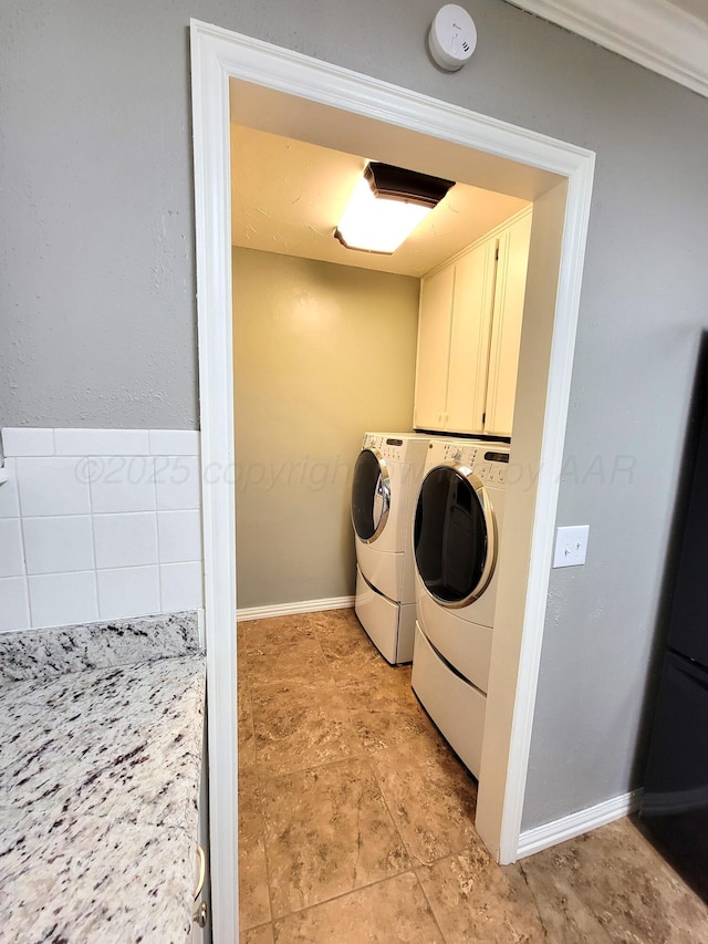 laundry area featuring light tile patterned floors, baseboards, cabinet space, and washer and clothes dryer