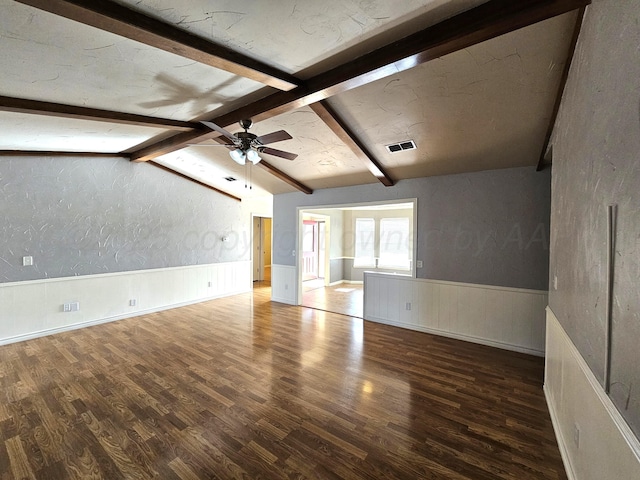 empty room featuring wood finished floors, visible vents, vaulted ceiling with beams, ceiling fan, and wainscoting