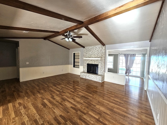 unfurnished living room with lofted ceiling with beams, a fireplace, wainscoting, ceiling fan, and dark wood-style flooring