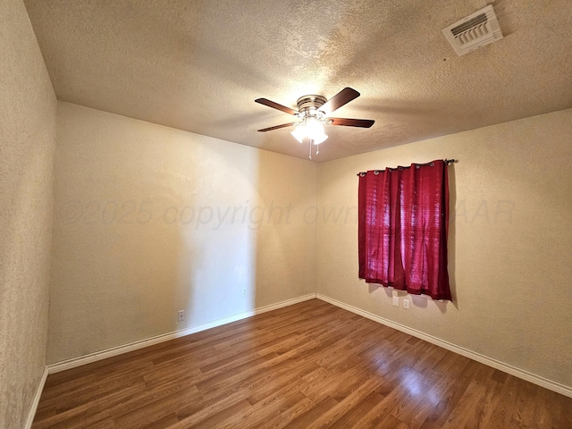 empty room featuring visible vents, a textured ceiling, wood finished floors, baseboards, and ceiling fan