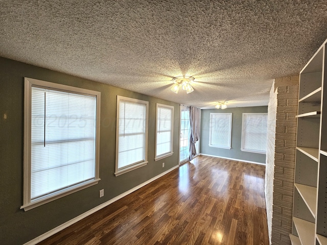 empty room featuring a textured ceiling, dark wood-type flooring, and baseboards