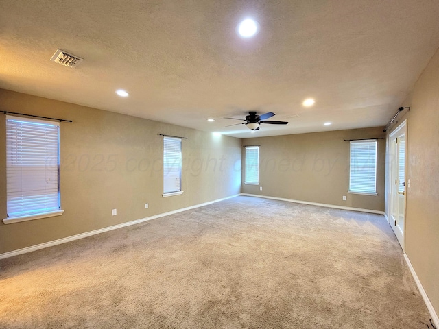 spare room with a textured ceiling, baseboards, visible vents, and light carpet