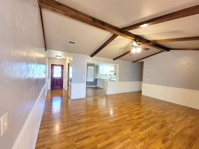 unfurnished living room with visible vents, ceiling fan, lofted ceiling with beams, wainscoting, and wood finished floors