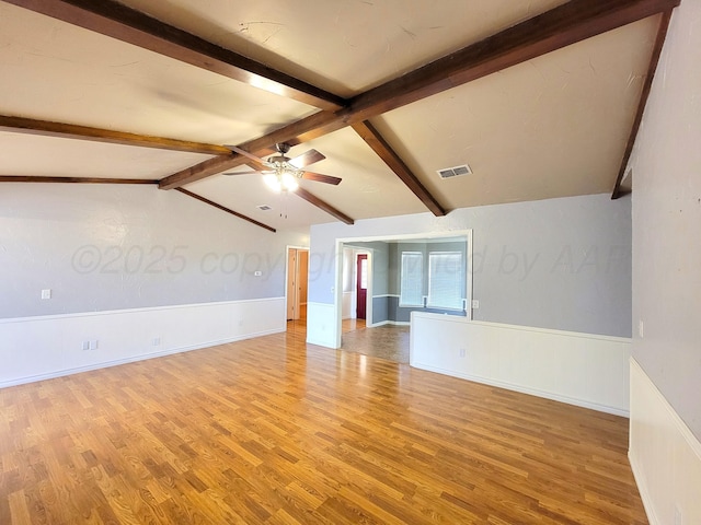 empty room with light wood finished floors, visible vents, vaulted ceiling with beams, a wainscoted wall, and a ceiling fan