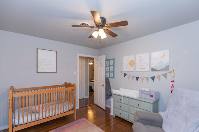 bedroom with wood finished floors, ceiling fan, a crib, and baseboards