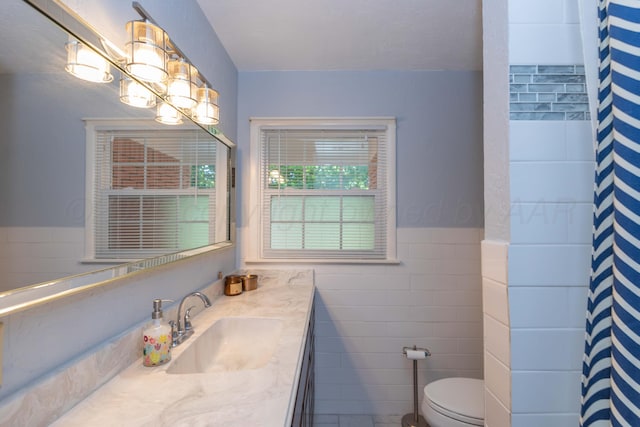 bathroom with toilet, tile walls, vanity, a wainscoted wall, and curtained shower