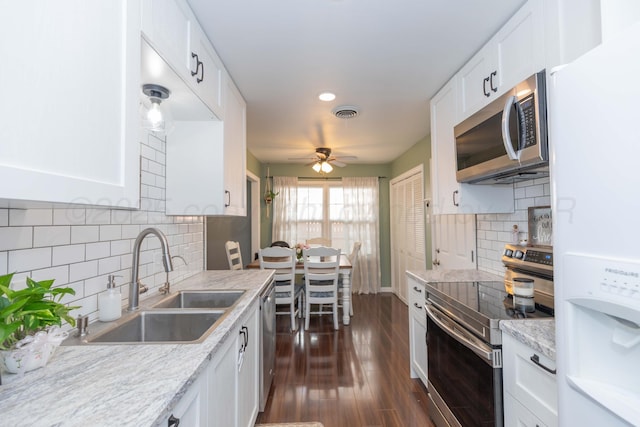 kitchen with stainless steel appliances, a sink, ceiling fan, white cabinetry, and decorative backsplash