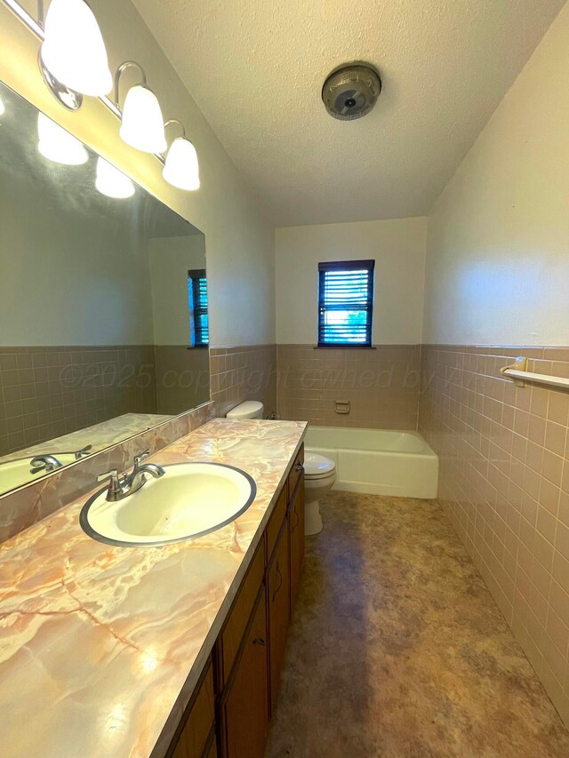 708 N Arizona St, Shamrock, TX 79079 - bathroom featuring tile walls, vanity, a textured ceiling, wainscoting, and a bathtub