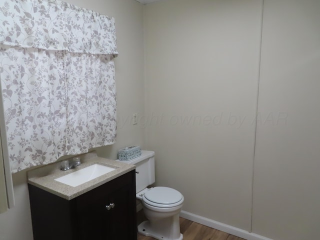 half bath with toilet, wood finished floors, and vanity