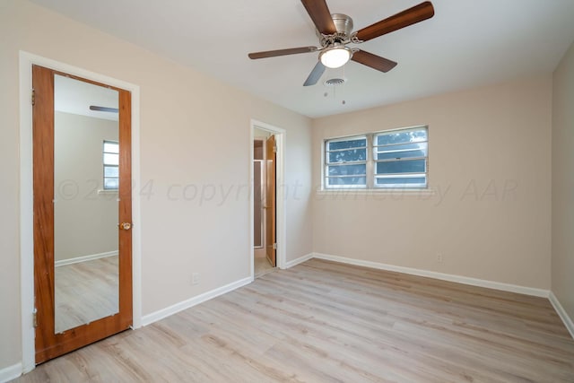 unfurnished bedroom with connected bathroom, light wood-type flooring, multiple windows, and ceiling fan