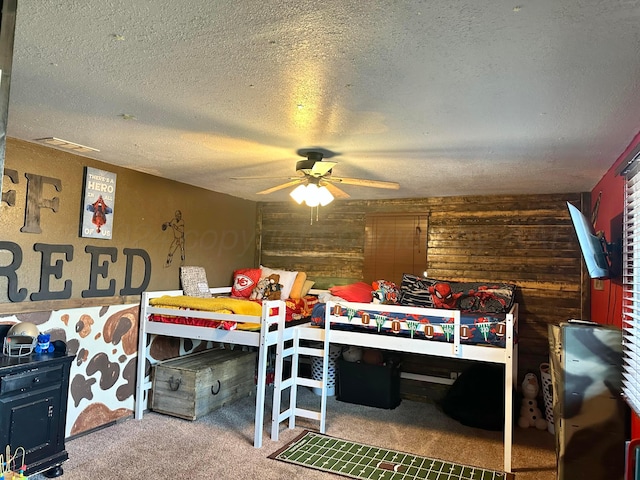 carpeted bedroom featuring ceiling fan, a textured ceiling, and wooden walls