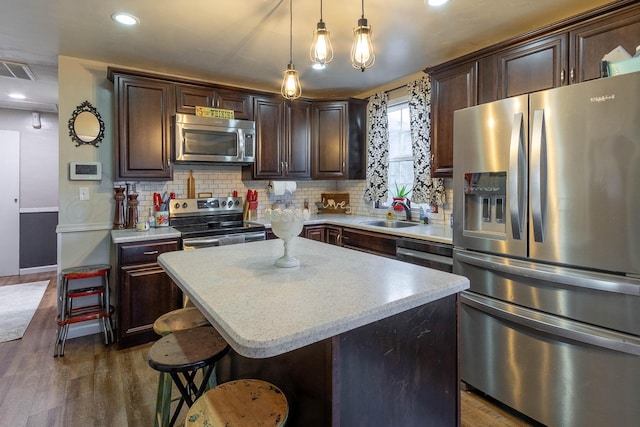 kitchen with appliances with stainless steel finishes, dark wood-type flooring, sink, pendant lighting, and a kitchen island