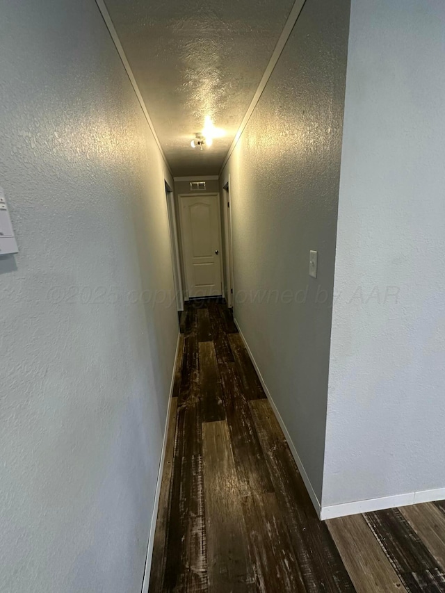 corridor with baseboards, ornamental molding, dark wood-style flooring, and a textured wall