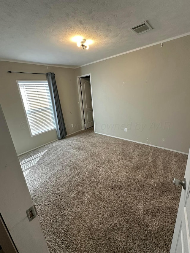 carpeted spare room featuring a textured ceiling, baseboards, visible vents, and crown molding