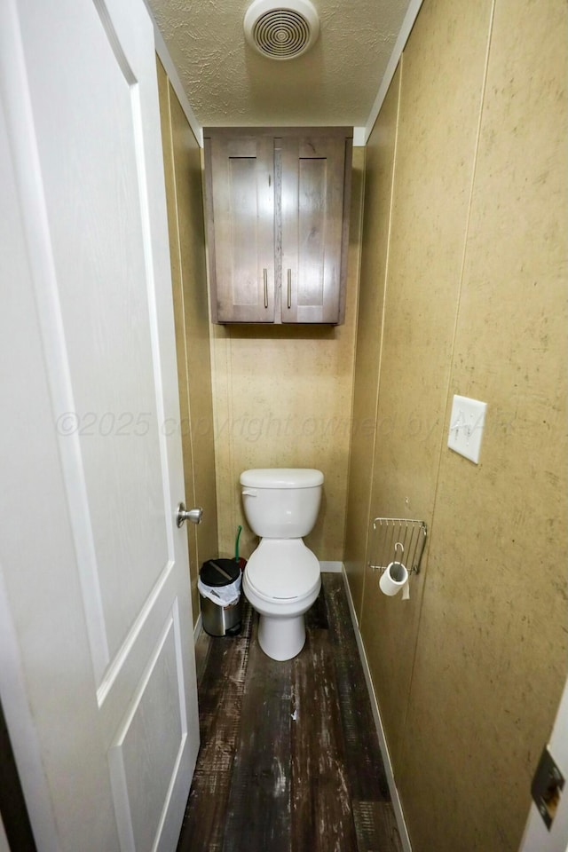 bathroom with a textured ceiling, toilet, wood finished floors, visible vents, and baseboards