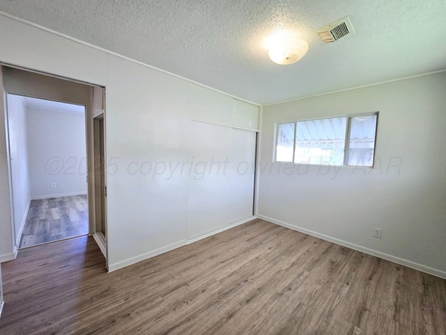unfurnished bedroom featuring visible vents, baseboards, a closet, a textured ceiling, and wood finished floors