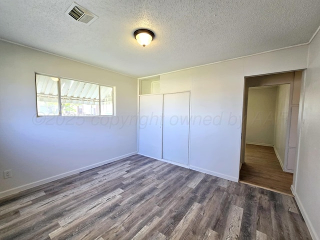 unfurnished bedroom featuring a closet, baseboards, a textured ceiling, visible vents, and wood finished floors