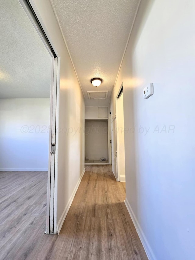corridor with a textured ceiling, baseboards, and wood finished floors
