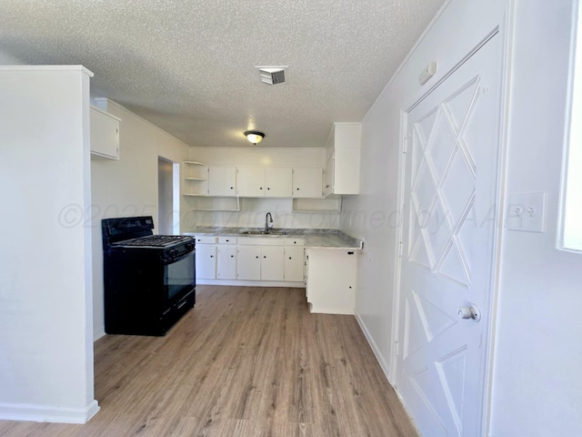 kitchen featuring light wood-style flooring, light countertops, a textured ceiling, black gas range oven, and a sink