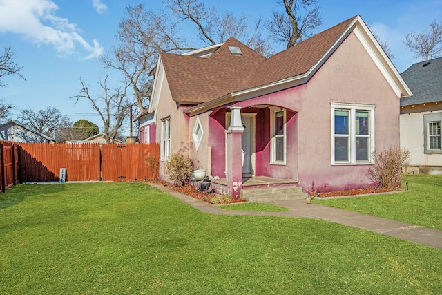 view of front of property featuring a front lawn, a shingled roof, fence, and stucco siding