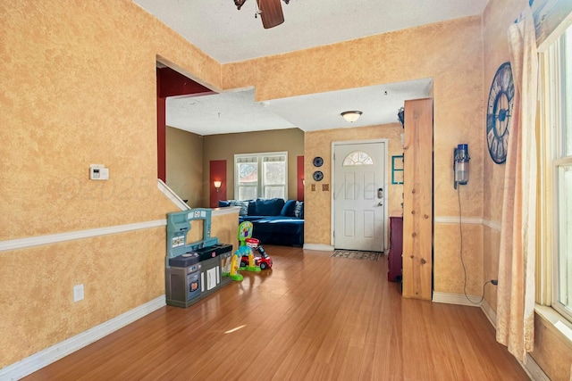 foyer entrance featuring a ceiling fan, wallpapered walls, baseboards, and wood finished floors