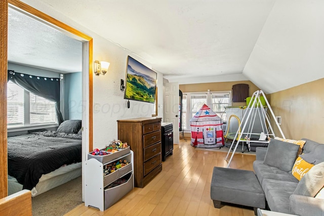 bedroom with lofted ceiling, a textured wall, a textured ceiling, and light wood-style flooring