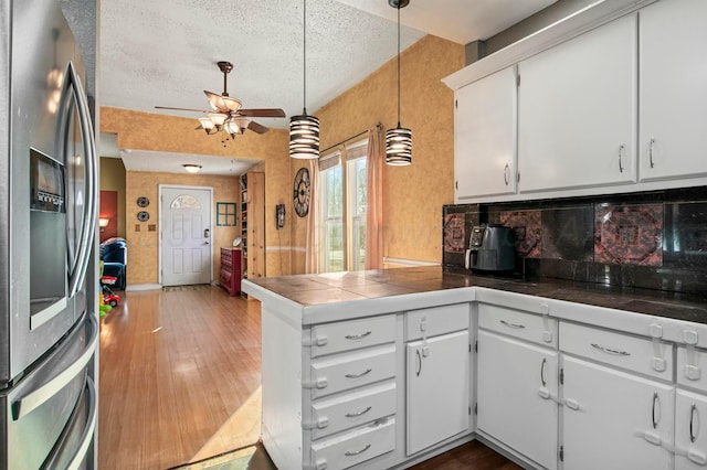 kitchen with a textured ceiling, a peninsula, wood finished floors, white cabinets, and stainless steel refrigerator with ice dispenser