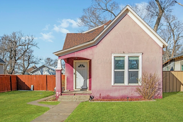 view of front of house with a shingled roof, a front yard, fence, and stucco siding