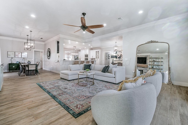 living room with crown molding, ceiling fan with notable chandelier, and light wood-type flooring