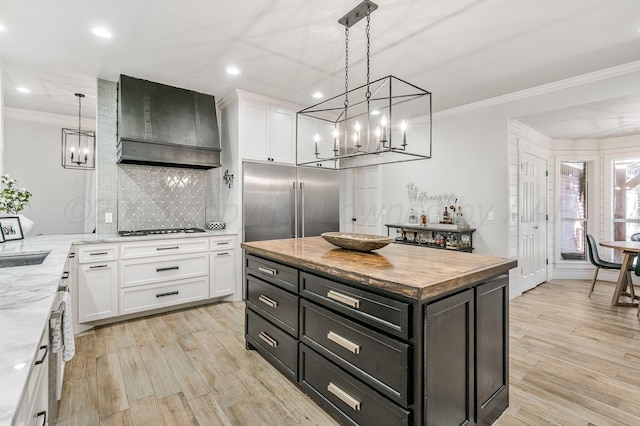 kitchen with premium range hood, decorative light fixtures, a center island, stainless steel appliances, and white cabinets