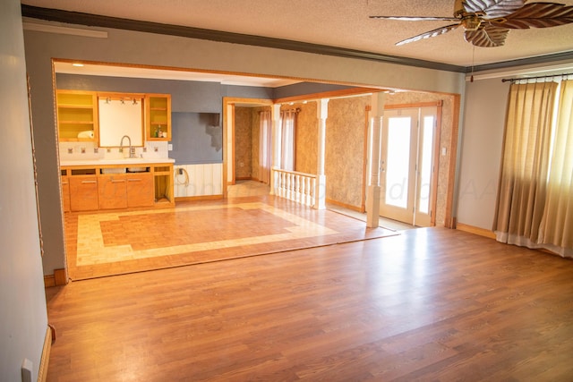 unfurnished living room with sink, crown molding, light hardwood / wood-style flooring, ceiling fan, and a textured ceiling