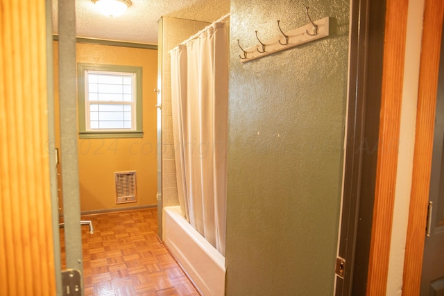 bathroom with parquet flooring, shower / tub combo, and a textured ceiling