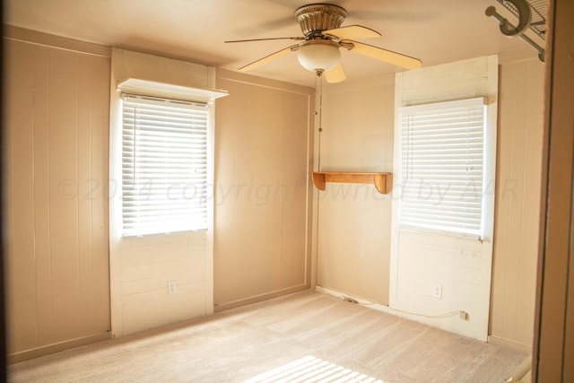 carpeted spare room featuring ceiling fan and wood walls