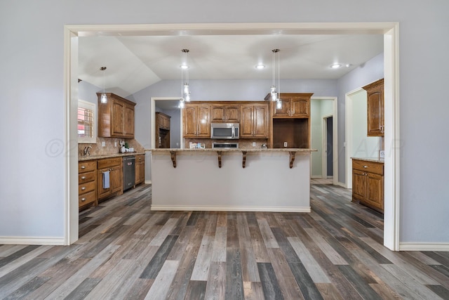 kitchen with brown cabinetry, dark wood-style flooring, a kitchen bar, stainless steel microwave, and tasteful backsplash