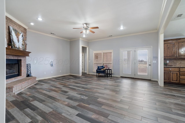 unfurnished living room featuring wood finished floors, visible vents, ceiling fan, crown molding, and a brick fireplace