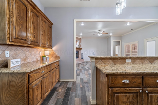 kitchen with a ceiling fan, light stone counters, backsplash, dark wood finished floors, and crown molding