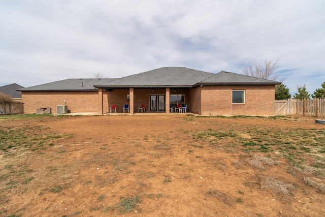 rear view of house with cooling unit, fence, roof with shingles, a patio area, and brick siding