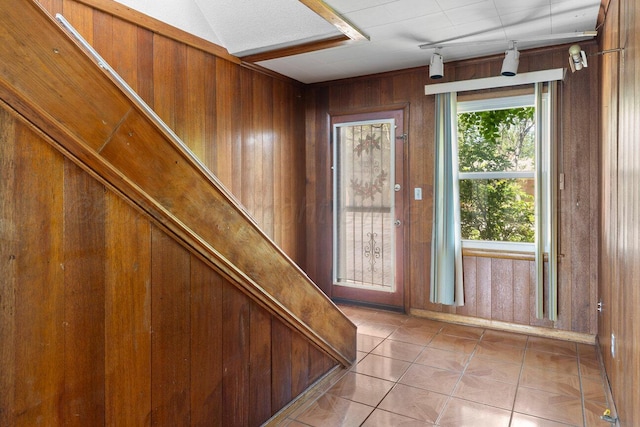 doorway with wood walls, light tile patterned floors, and baseboards