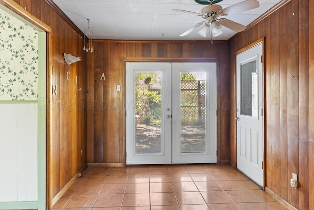 doorway with french doors, wooden walls, light tile patterned floors, ceiling fan, and baseboards
