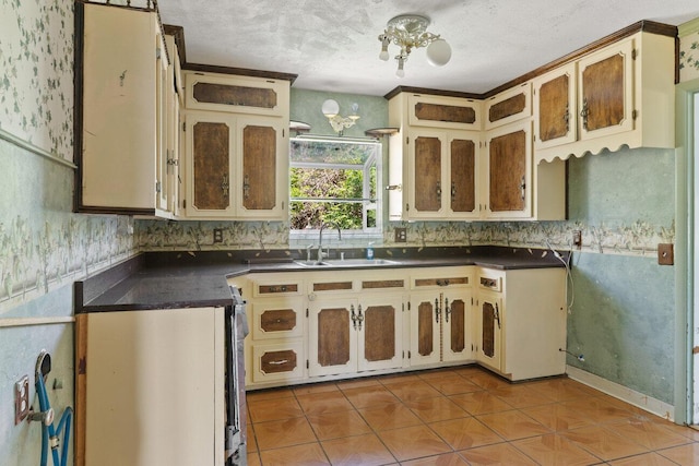 kitchen with dark countertops, light tile patterned floors, a sink, a textured ceiling, and a chandelier