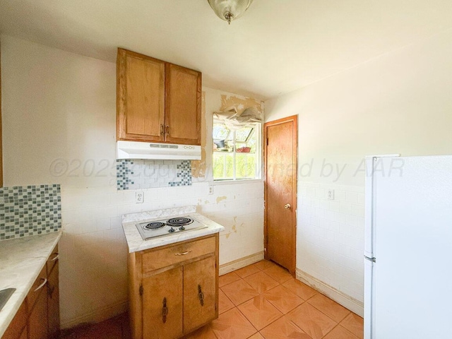 kitchen featuring freestanding refrigerator, under cabinet range hood, electric stovetop, light countertops, and tile walls