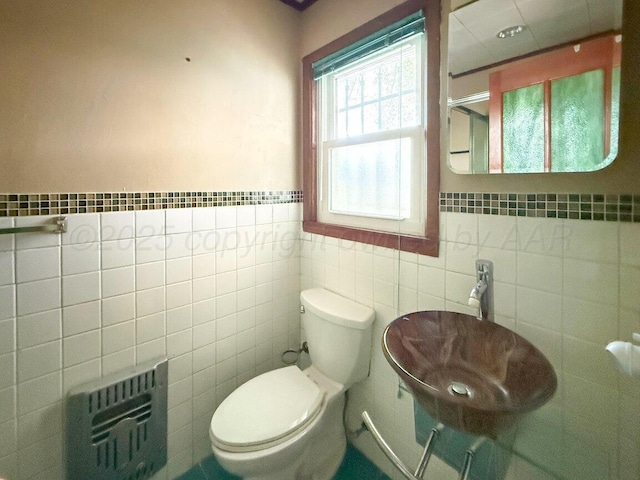 bathroom featuring tile walls, heating unit, toilet, a sink, and a wainscoted wall