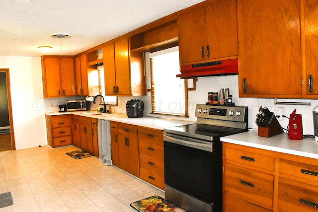 501 Bruce Ave, Dumas, TX 79029 - kitchen with appliances with stainless steel finishes, under cabinet range hood, light countertops, tasteful backsplash, and brown cabinetry