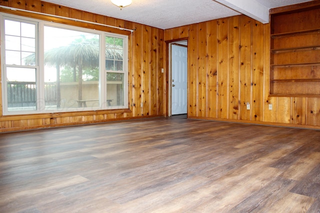 219 Kiekbusch St, Borger, TX 79007 - unfurnished room featuring wooden walls, a textured ceiling, beamed ceiling, and wood finished floors