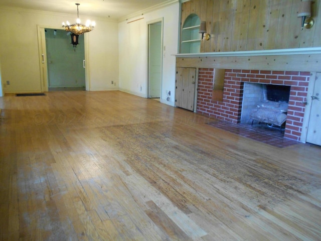 unfurnished living room featuring ornamental molding, an inviting chandelier, wood-type flooring, and a brick fireplace