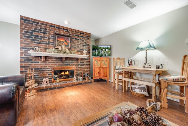 living room featuring lofted ceiling, visible vents, ornamental molding, a brick fireplace, and wood finished floors