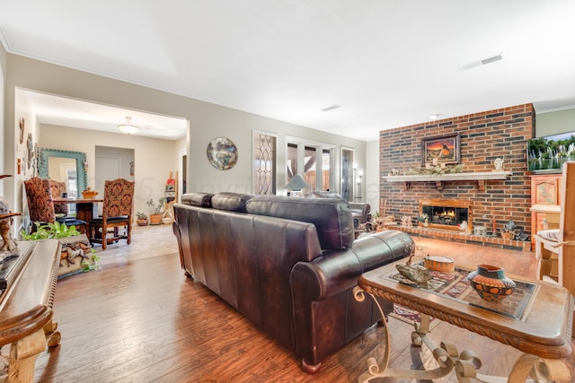 living area with ornamental molding, a brick fireplace, visible vents, and wood-type flooring