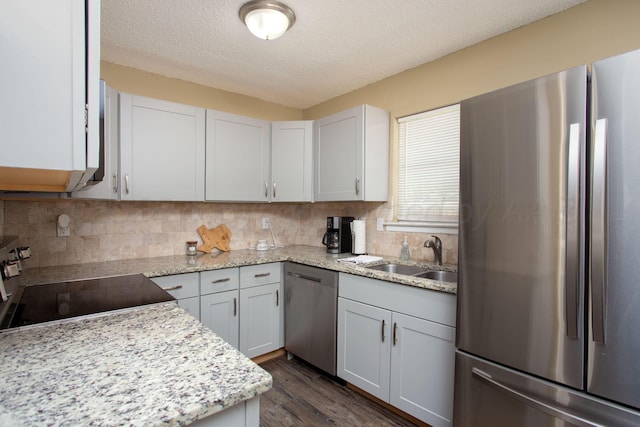 kitchen with appliances with stainless steel finishes, a sink, dark wood-style flooring, decorative backsplash, and a textured ceiling