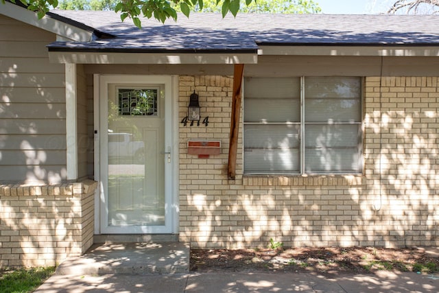 property entrance featuring brick siding and a shingled roof