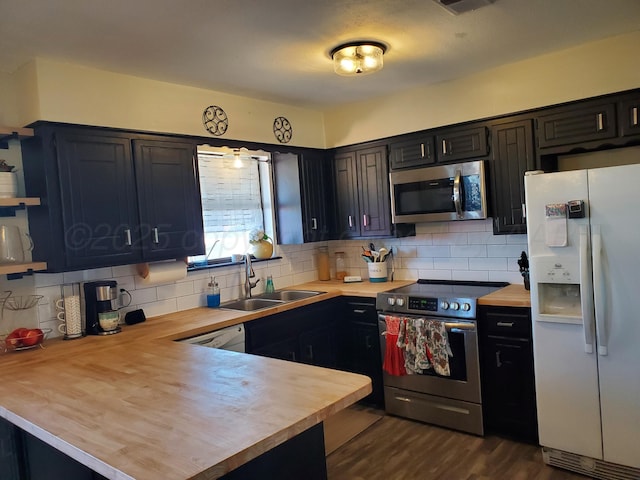 kitchen featuring backsplash, butcher block counters, a peninsula, stainless steel appliances, and a sink